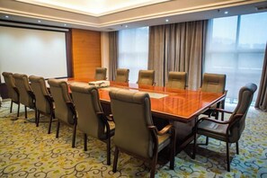 Un salón de conferencias con una larga mesa, varias sillas, una pantalla de proyector y un amplio ventanal con cortinas.