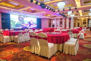 A banquet hall with round tables, white chairs, and a stage with a large screen. - Xiangsihu International Hotel (Nanning)