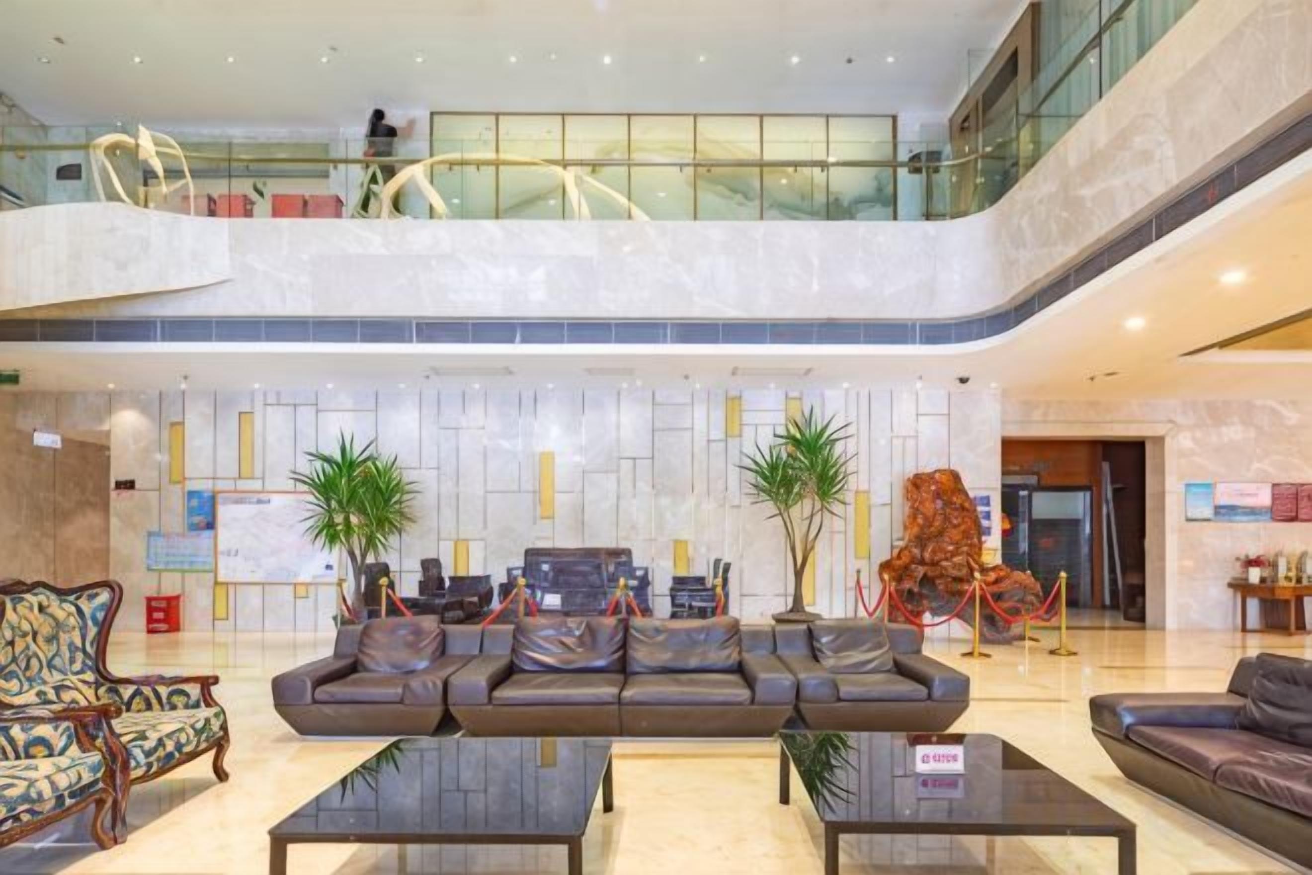Een ruime lobby met een hoge plafond, zithoek en een glazen balustrade met uitzicht op de verdieping daaronder.