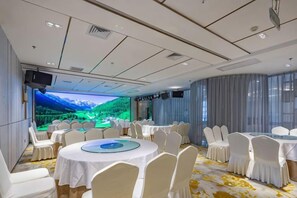 Un salón de conferencias con mesas redondas, sillas blancas, una pantalla grande y una vista panorámica.