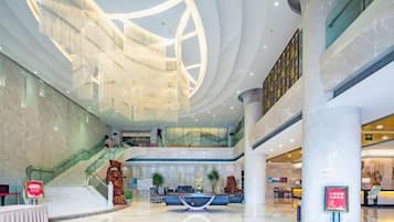 A spacious lobby with a central reception desk, a staircase, and a glass ceiling.