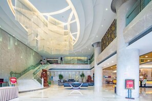 Un hall d’entrée spacieux avec un comptoir d’accueil central, un escalier et un plafond en verre.