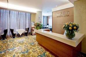 Ein Hotel-Rezeptionsbereich mit Empfangsschalter, einer Sitzecke mit Stühlen und einem großen Fenster mit Vorhängen.