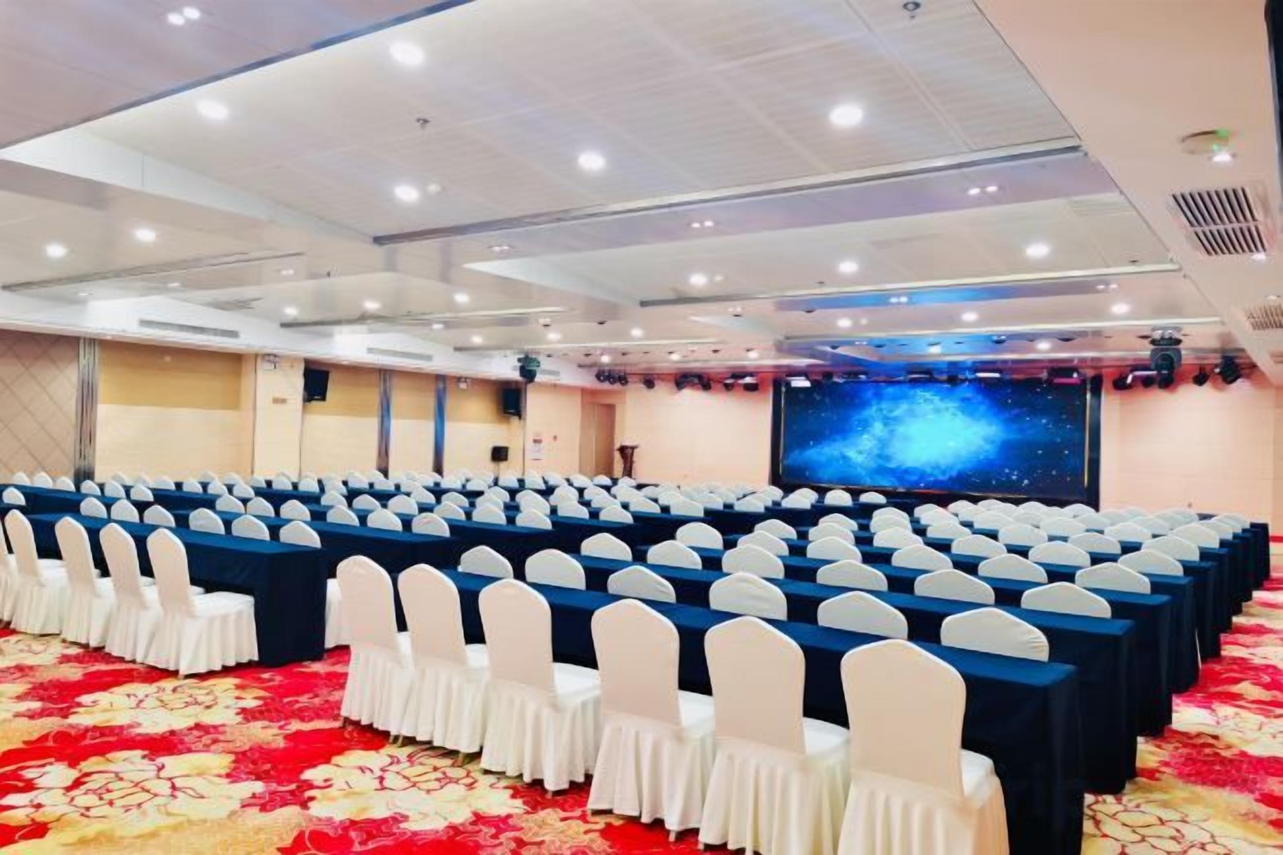 A conference room with rows of chairs, a stage, and a large screen.