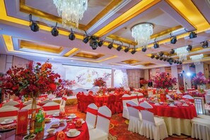 Een balzaal met ronde tafels, stoelen en bloemdecoraties.