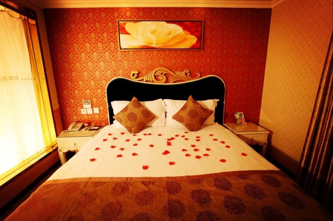 A hotel room with a large bed, a headboard with decorative carvings, two bedside tables, a telephone, and a framed picture on the wall.