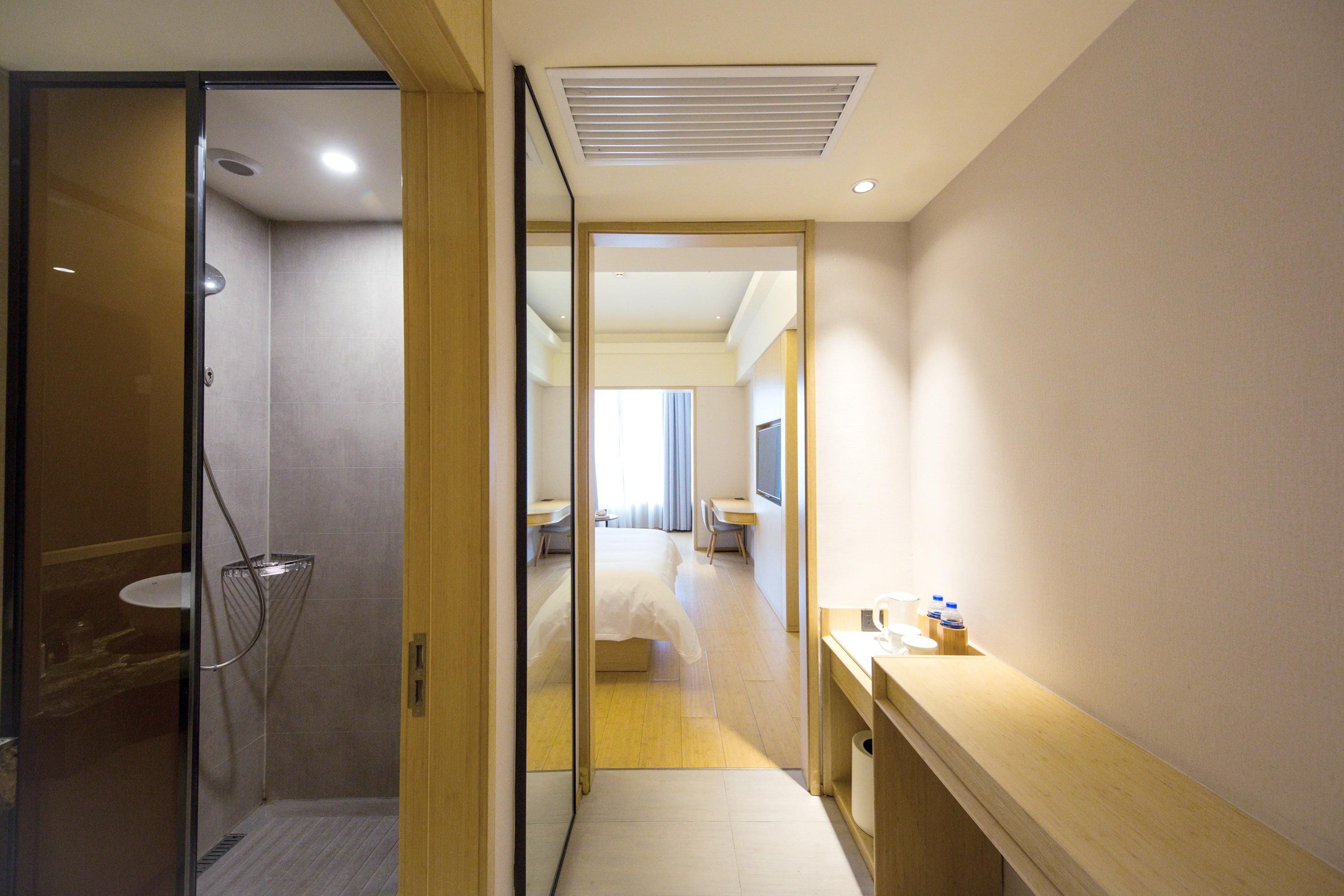 Habitación de hotel con ducha, escritorio, cama y vista al pasillo.