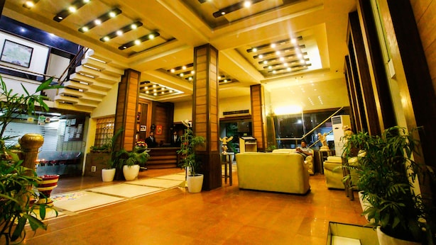 A hotel lobby with a staircase, seating area, and potted plants. - Hotel Rishi Regency (Jabalpur)