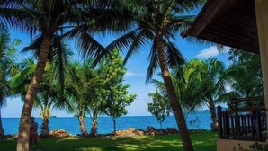 A tropical setting with palm trees, a clear view of the ocean, and a building with a covered porch. - Coral Resort (Ko Chang)