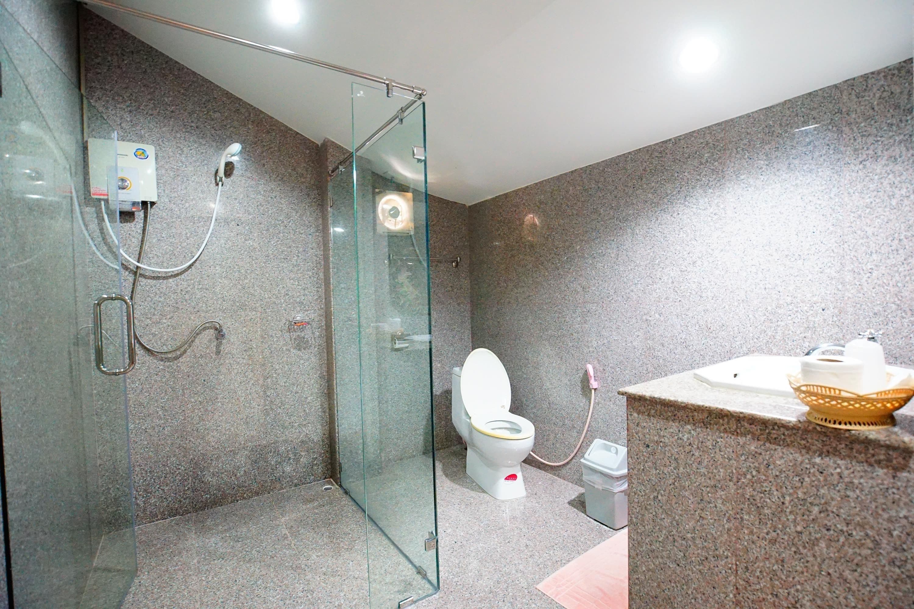 Une salle de bain moderne dotée d’une douche à parois de verre, de toilettes et d’un comptoir en granit avec un évier et un bol décoratif.