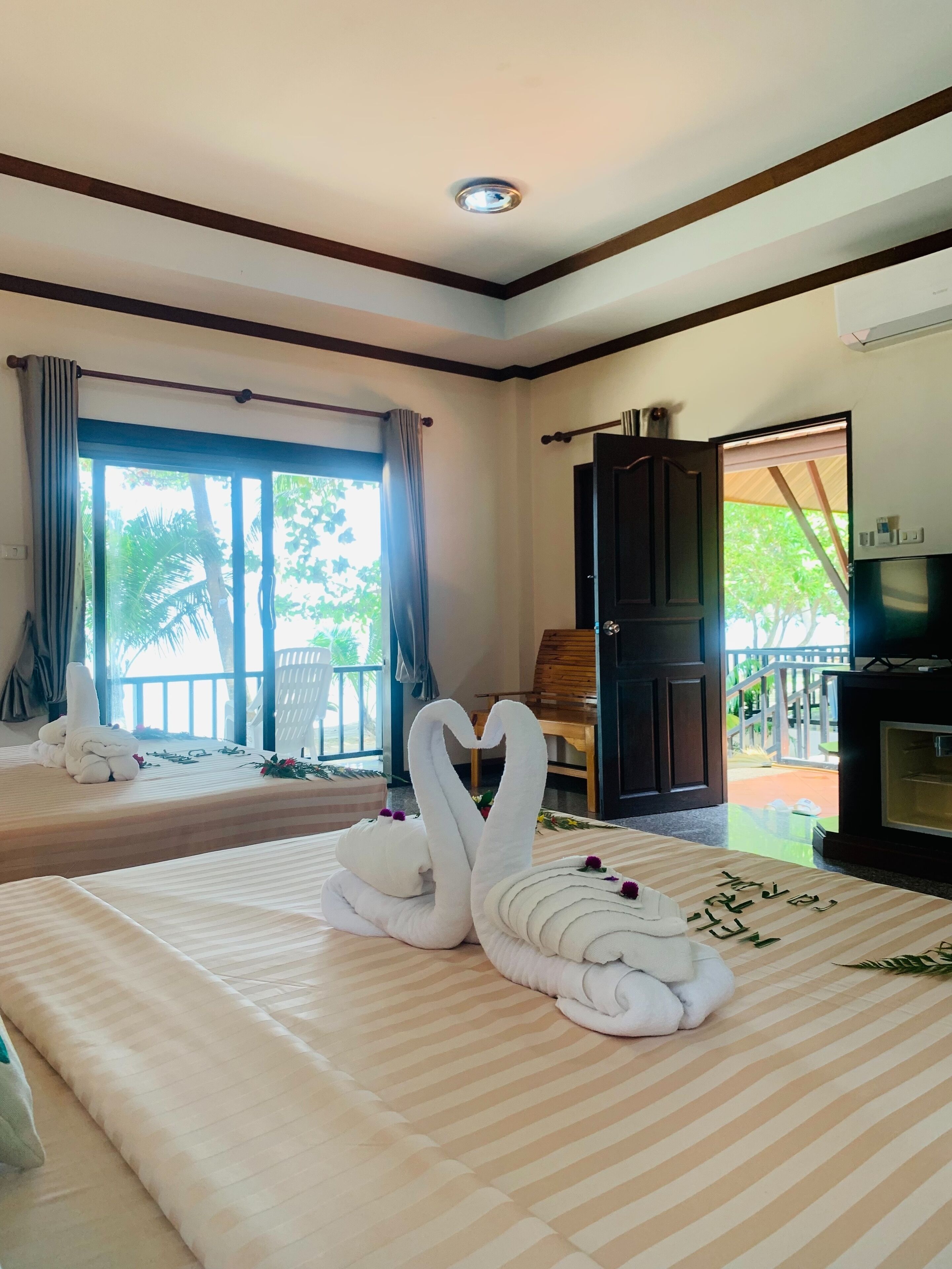 A hotel room with two beds, a balcony, a fireplace, and a view of greenery.