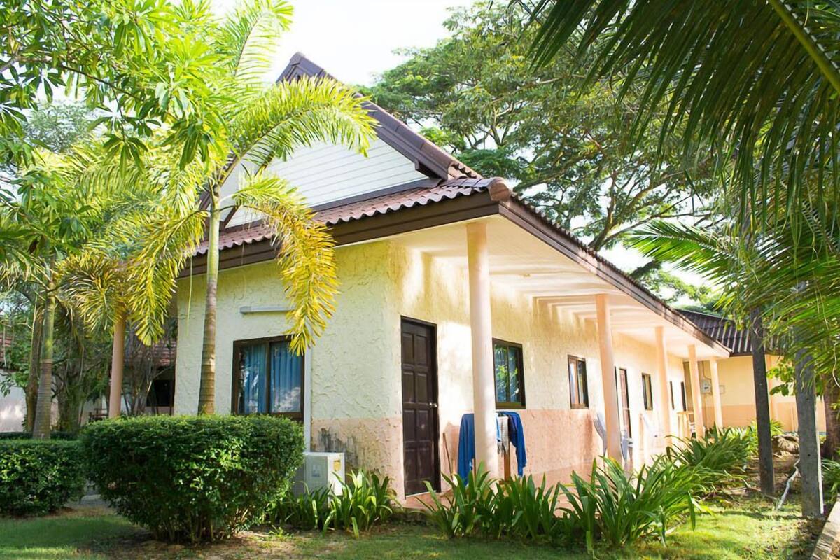 Un bâtiment à deux étages, doté d’un toit en tuiles, entouré d’une végétation luxuriante et de palmiers.