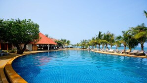 A swimming pool with a tiled edge, surrounded by lounge chairs and palm trees, with a building featuring a red roof in the background. - Coral Resort (Ko Chang)