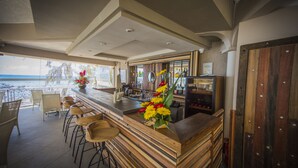 Una zona de bar con taburetes de madera, mostrador de madera y vista a la playa.