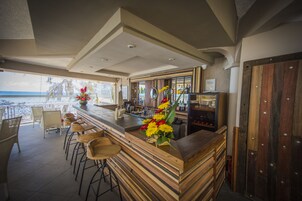 Una zona de bar con taburetes de madera, mostrador de madera y vista a la playa.