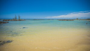 Una playa con agua turquesa cristalina, orilla arenosa y afloramientos rocosos.