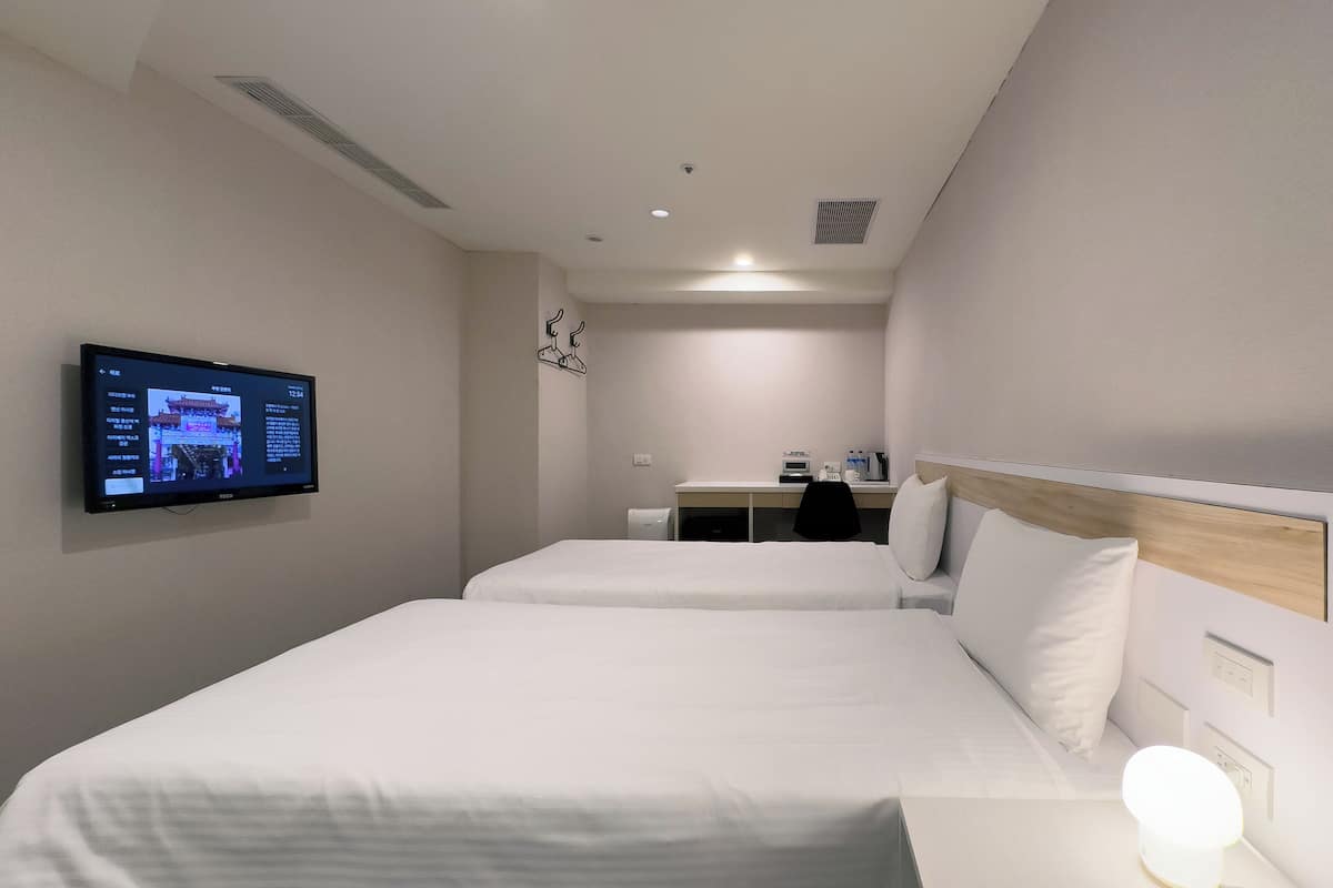 Habitación de hotel con dos camas, un escritorio, un televisor montado en la pared y un calentador también fijado a la pared.