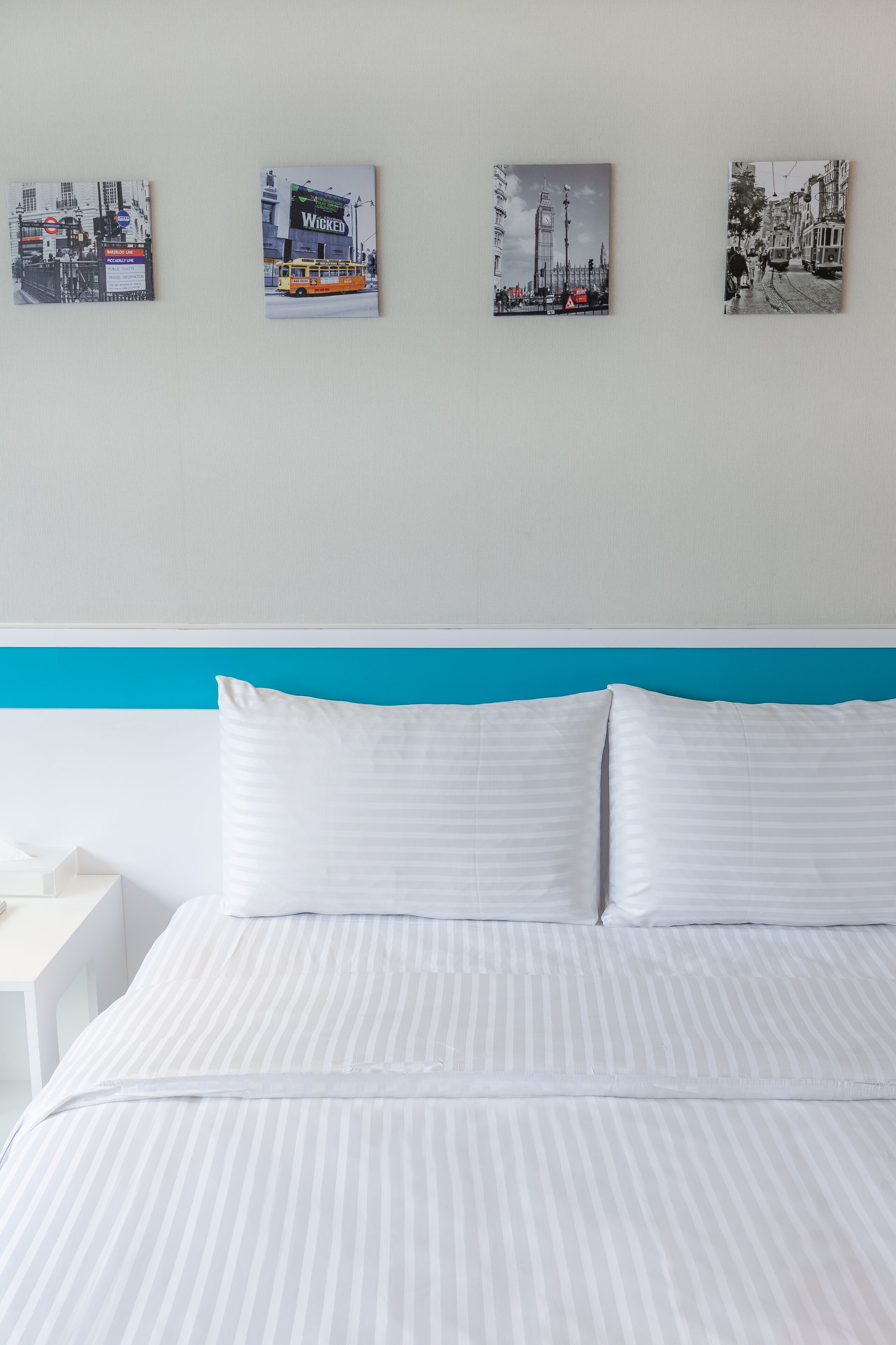 A hotel room with a bed, white pillows, a blue headboard, and three framed pictures on the wall.