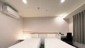 Une chambre d’hôtel avec deux lits simples, un bureau avec une chaise, un téléphone et un appareil de climatisation.