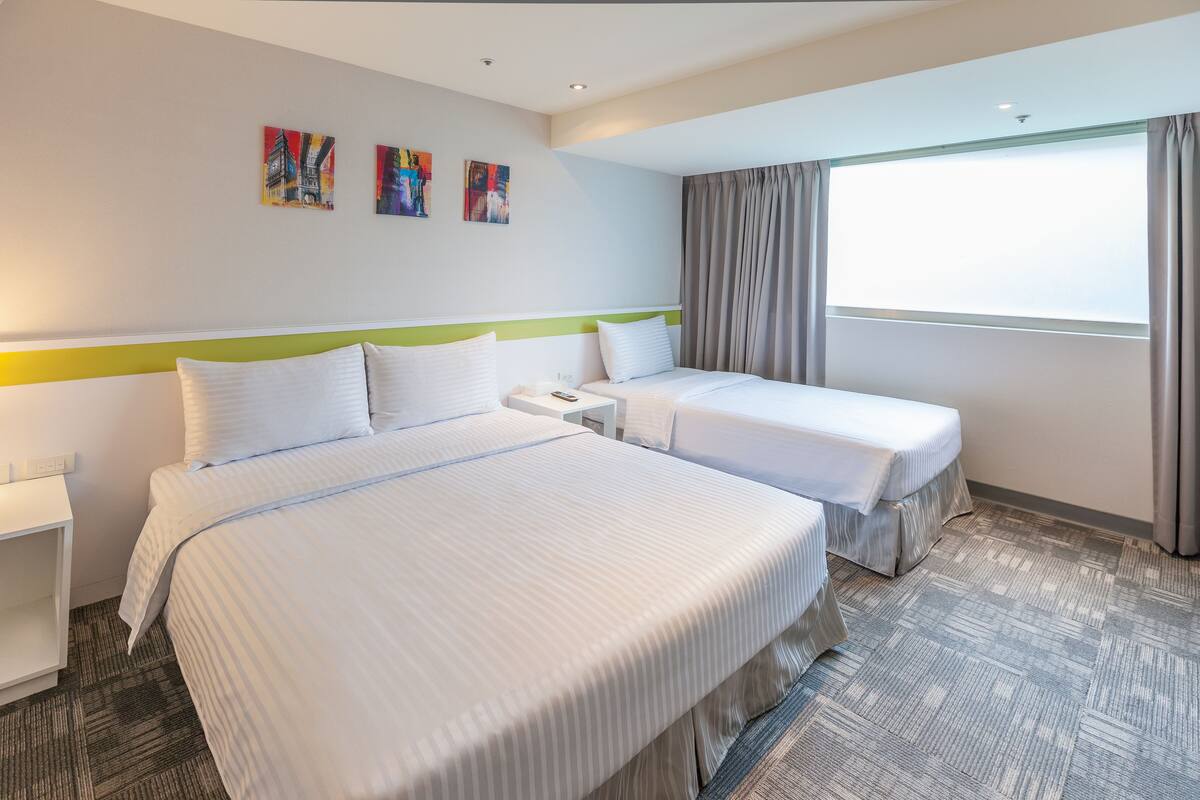 Habitación de hotel con dos camas, un ventanal con cortinas y obras de arte en la pared.