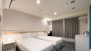 Une chambre d’hôtel avec deux lits, un bureau, une chaise, un petit réfrigérateur et une fenêtre avec des rideaux.
