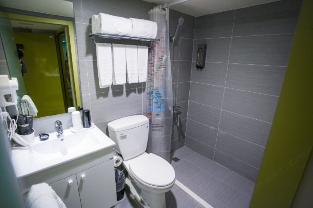 Een moderne badkamer met een wit wastafel, toilet en douche. Handdoeken hangen aan een rek en er is een spiegel boven het wastafel.