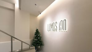 A modern hotel interior with a staircase, a Christmas tree, and a wall-mounted sign for 'LUMOS INN'. - LUMOS INN (Taipei)