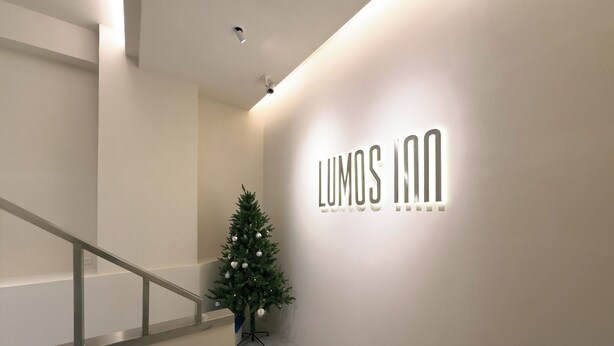 Un intérieur d’hôtel moderne avec un escalier, un sapin de Noël et une enseigne murale indiquant « LUMOS INN ».