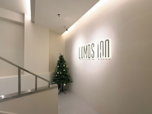 A modern hotel interior with a staircase, a Christmas tree, and a wall-mounted sign for 'LUMOS INN'. - LUMOS INN (Taipei)