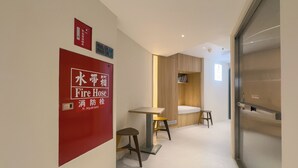 Un couloir avec un panneau indiquant l’emplacement d’une borne d’incendie, une petite table, deux tabourets et un meuble en bois.