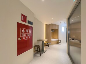 A hallway with a fire hose sign, a small table, two stools, and a wooden cabinet. - LUMOS INN (Taipei)