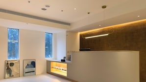 A reception area with a modern design, featuring a reception desk, a wooden accent wall, and two windows providing natural light. - LUMOS INN (Taipei)