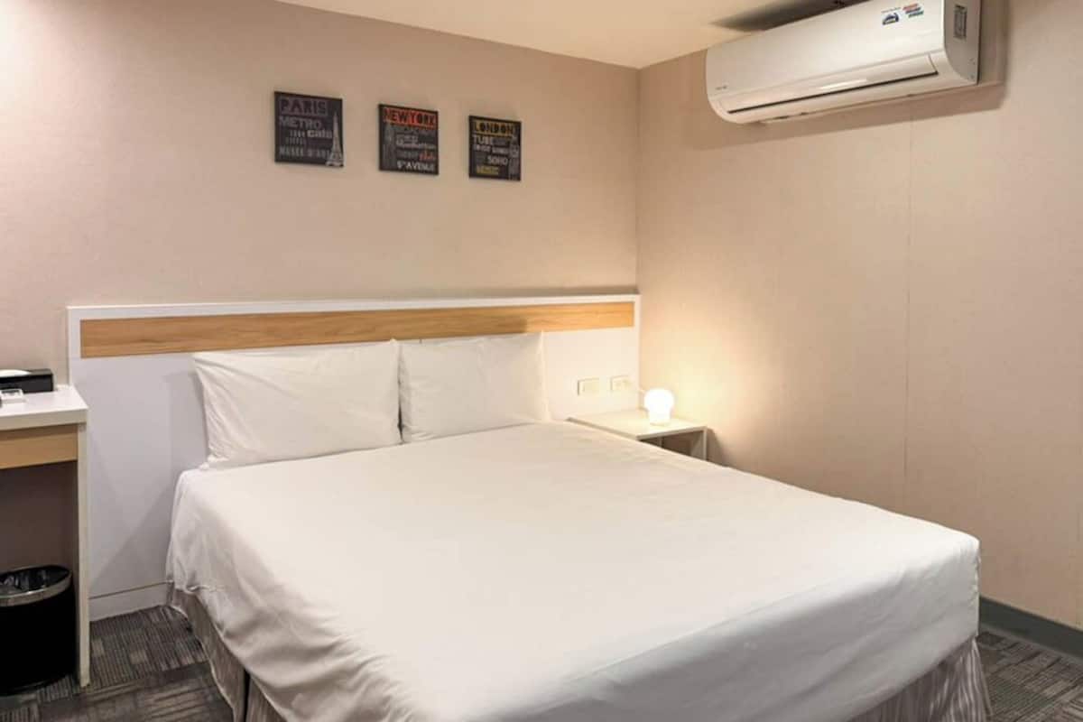 Una habitación de hotel con cama, mesita de noche, lámpara y aire acondicionado.