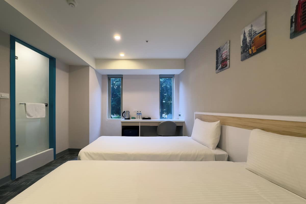 Una habitación de hotel moderna con dos camas, un escritorio y una ventana con vistas a árboles.