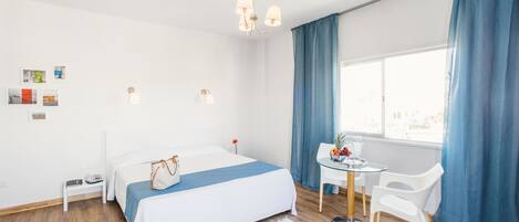 Une chambre d’hôtel moderne équipée d’un lit, d’une table de chevet, d’une chaise, d’un bureau et d’une fenêtre avec des rideaux.