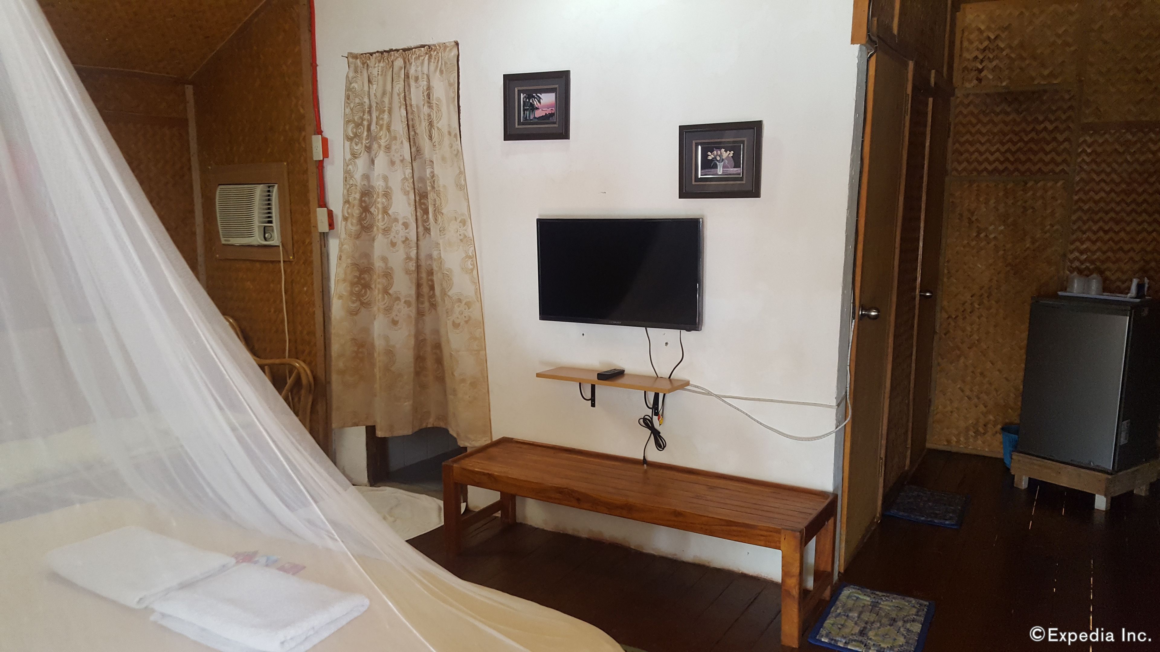 A bedroom with a bed, a TV mounted on the wall, a bedside table, and a bench.