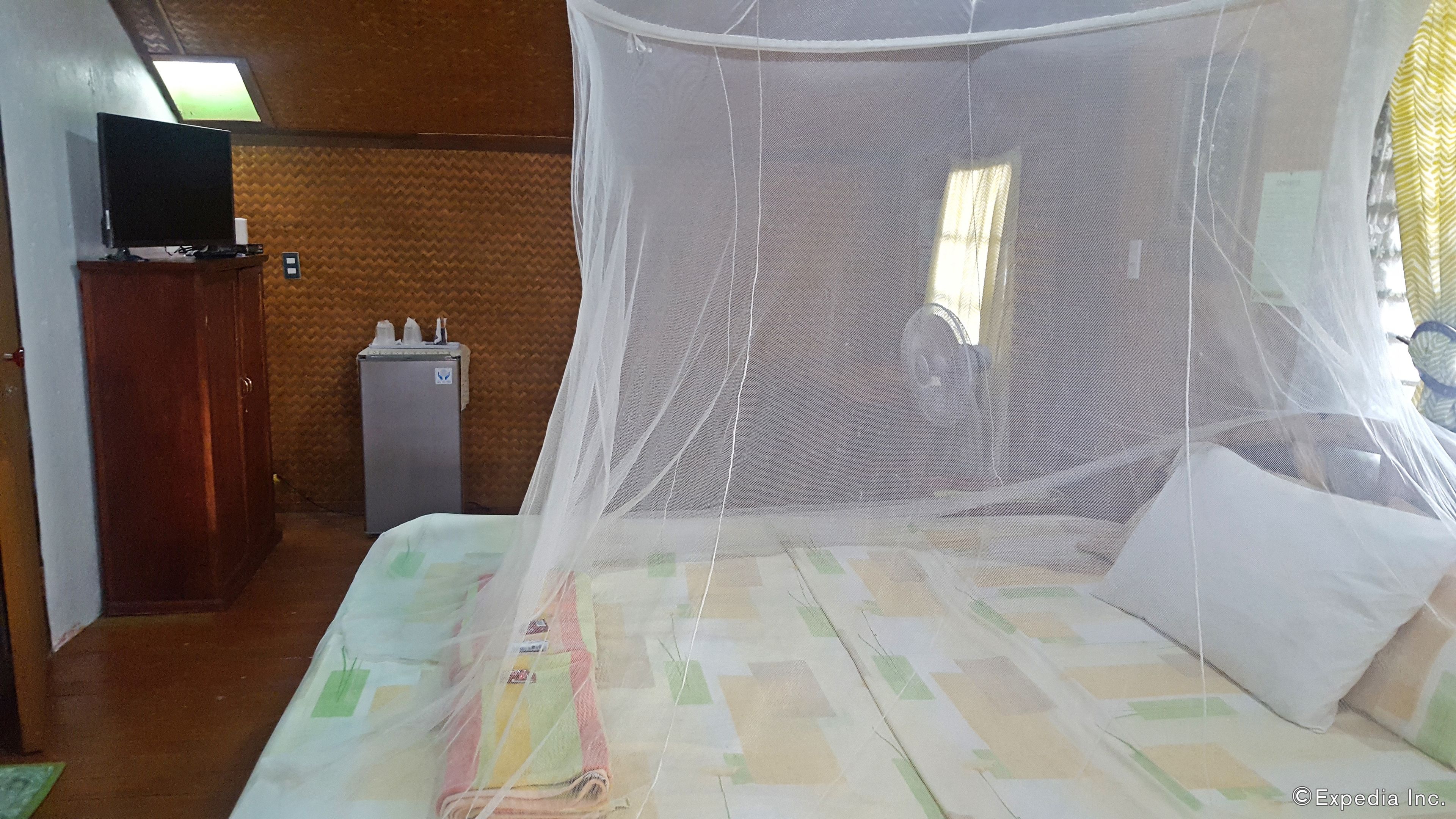 A room with a bed covered by a mosquito net, a television on a cabinet, and a refrigerator.