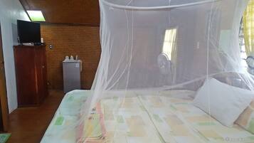 A room with a bed covered by a mosquito net, a television on a cabinet, and a refrigerator.