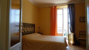 A bedroom with a bed, a nightstand, a window with curtains, and a chair.