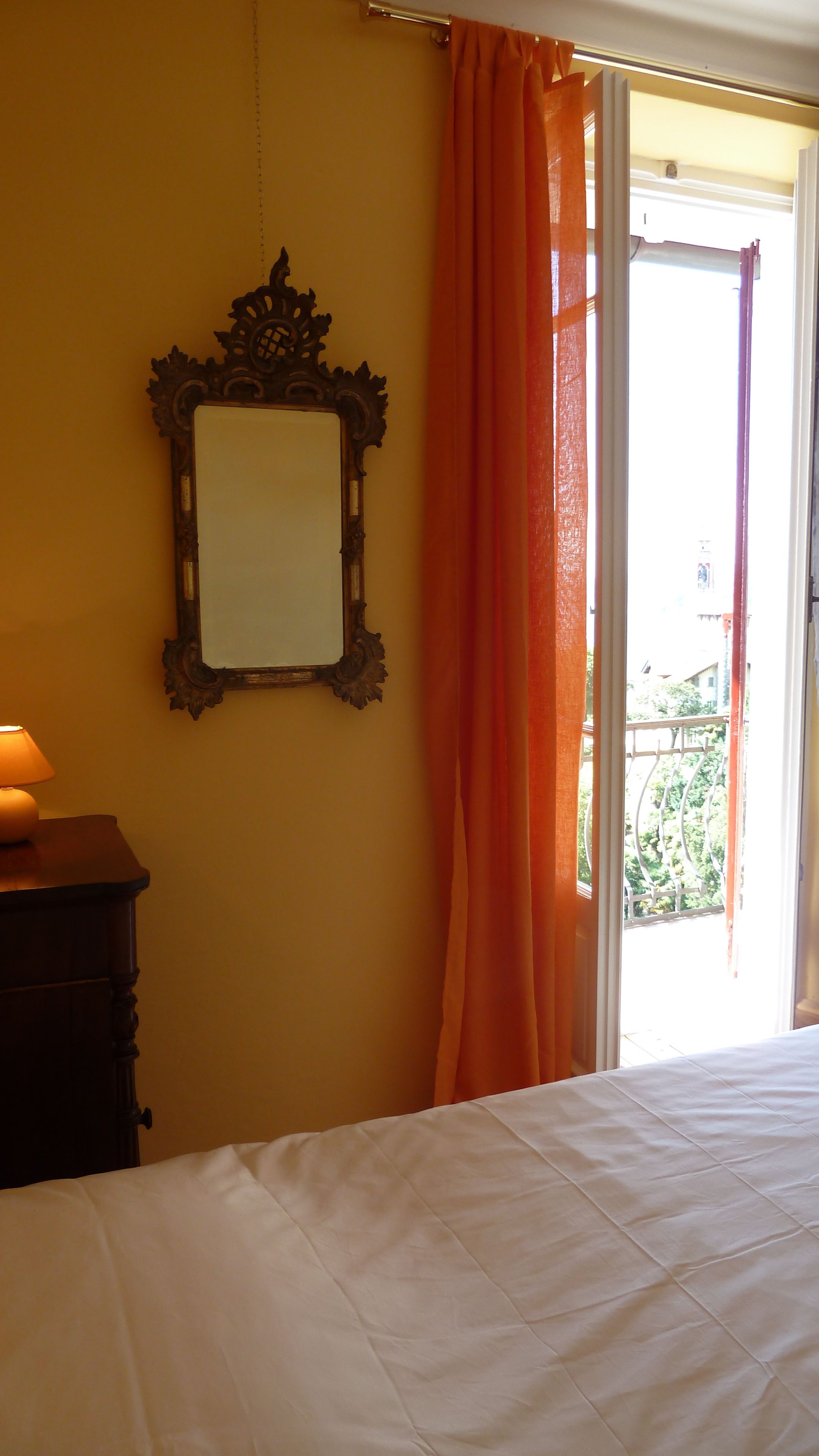 Een slaapkamer met een bed, een dressoir, een spiegel en een open slaande deur naar een balkon.