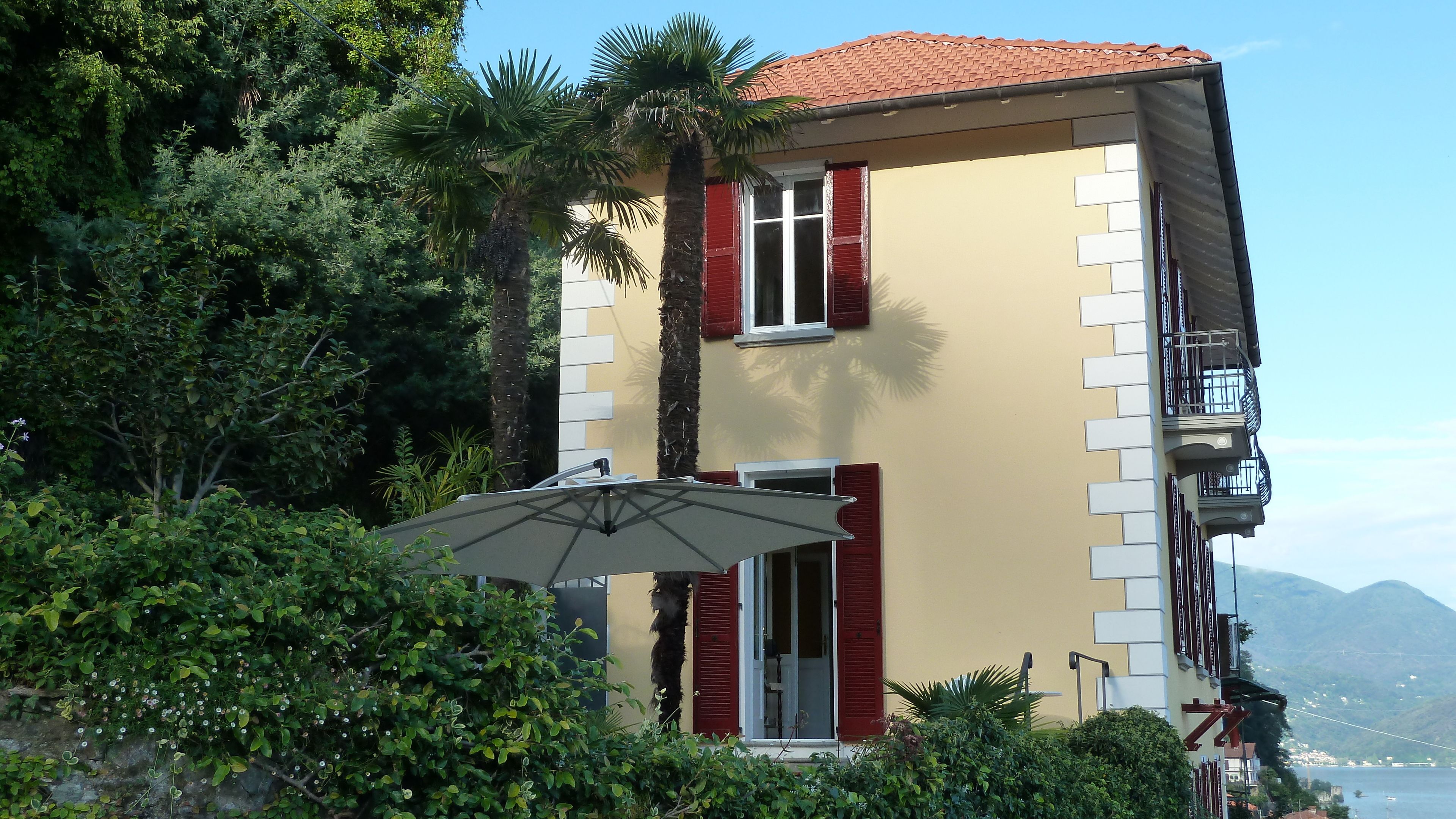 A two-story building with red shutters, a balcony, and a view of the sea.