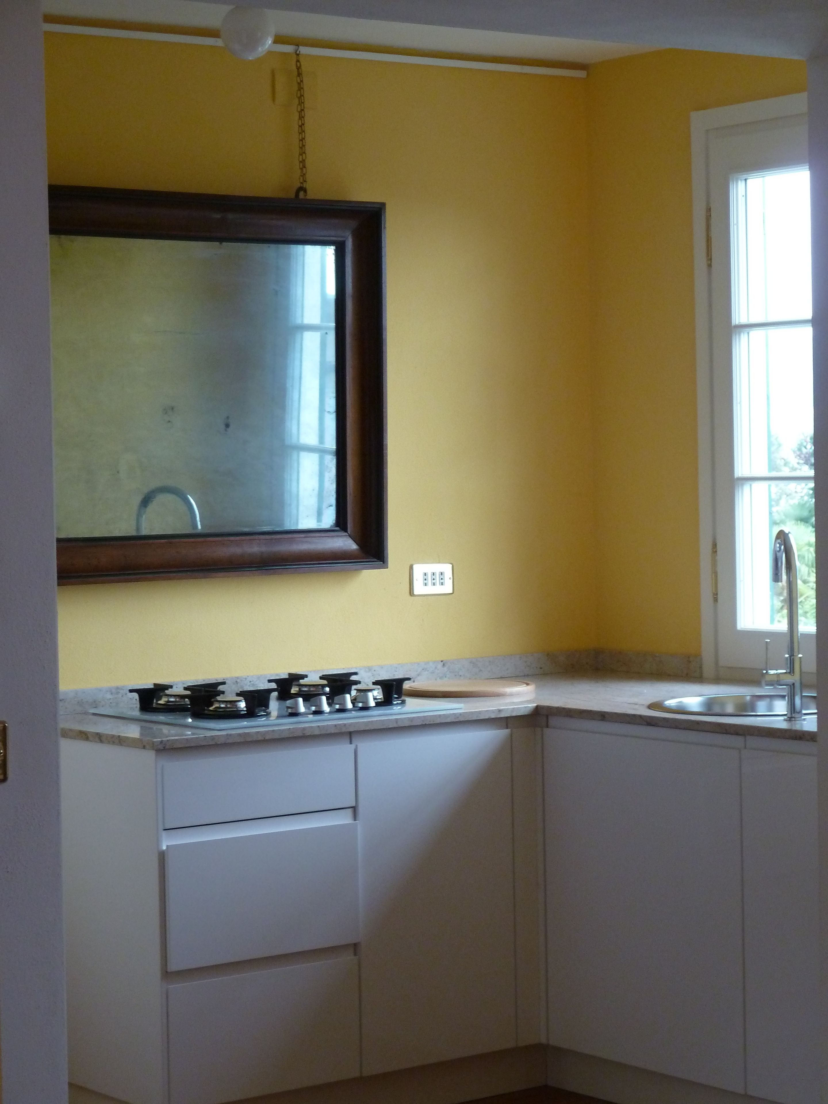 A kitchen with a gas stove, white cabinets, a window, and a mirror.