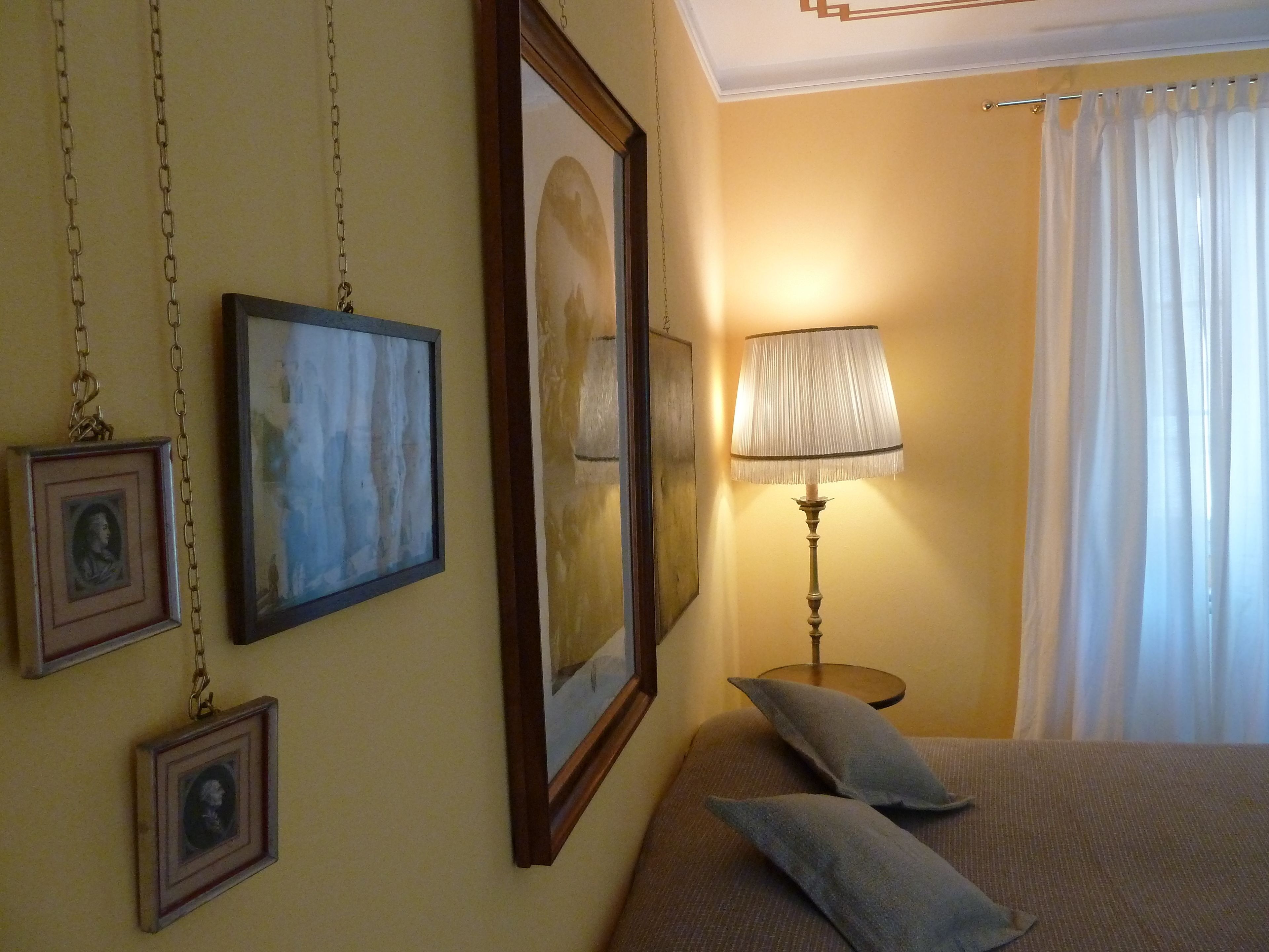 A bedroom with a bed, a lamp, and framed pictures on the wall.