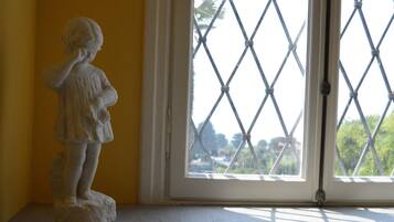 Une statue d’un enfant se trouve dans une pièce dotée d’une fenêtre ornée d’une grille à motifs losangés.