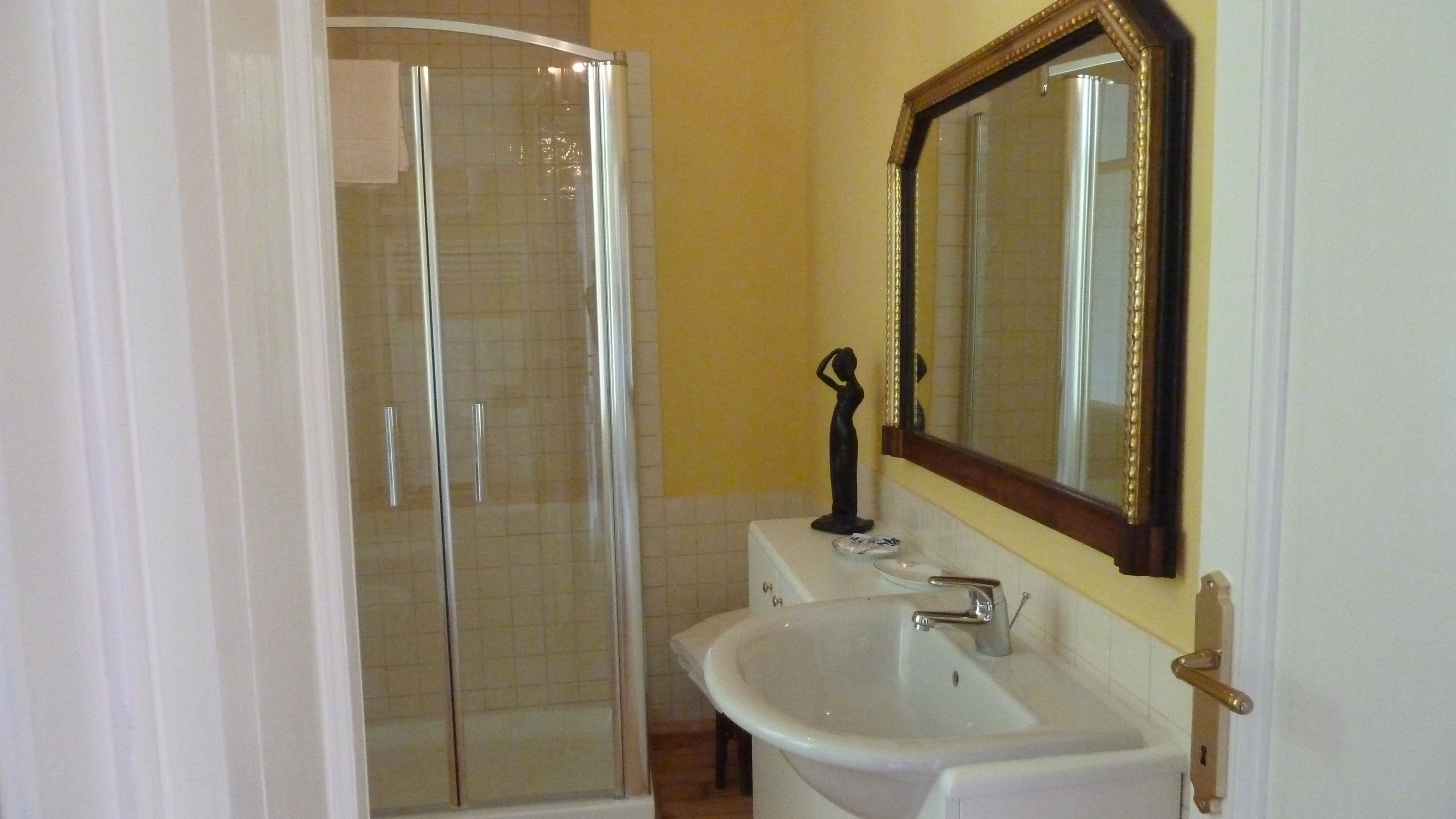 A bathroom with a glass shower enclosure, a white sink, and a mirror with a decorative frame.