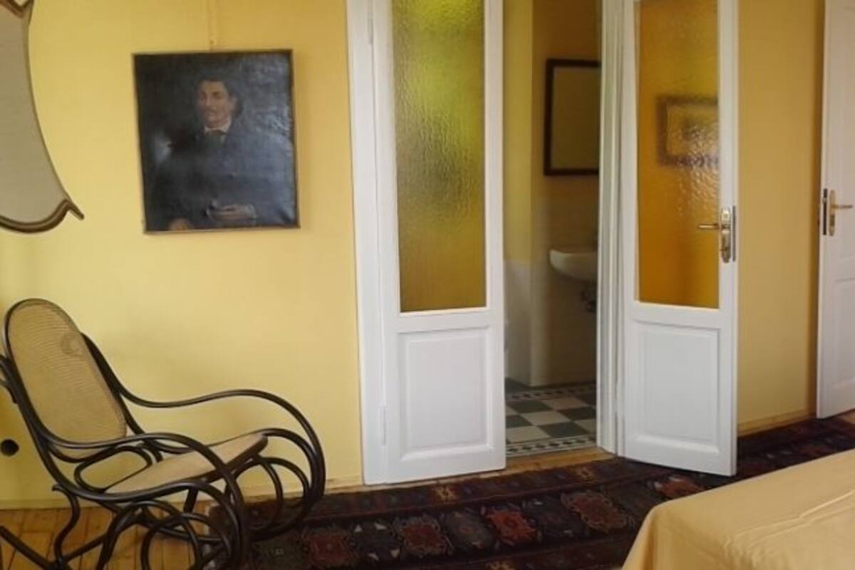 A bedroom with a bed, a chair, a nightstand, and a door leading to a bathroom.