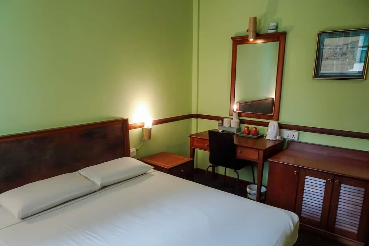 Habitación de hotel con cama, escritorio, silla, espejo y mesita de noche.