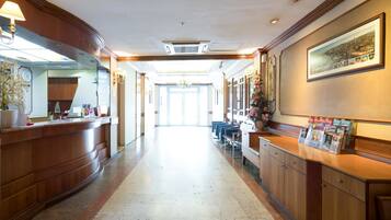 A hotel reception area with a wooden reception desk, a clock, and a framed cityscape picture on the wall.