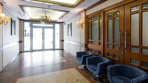 Een hotellobby met een kroonluchter, houten deuren en blauwe stoelen.