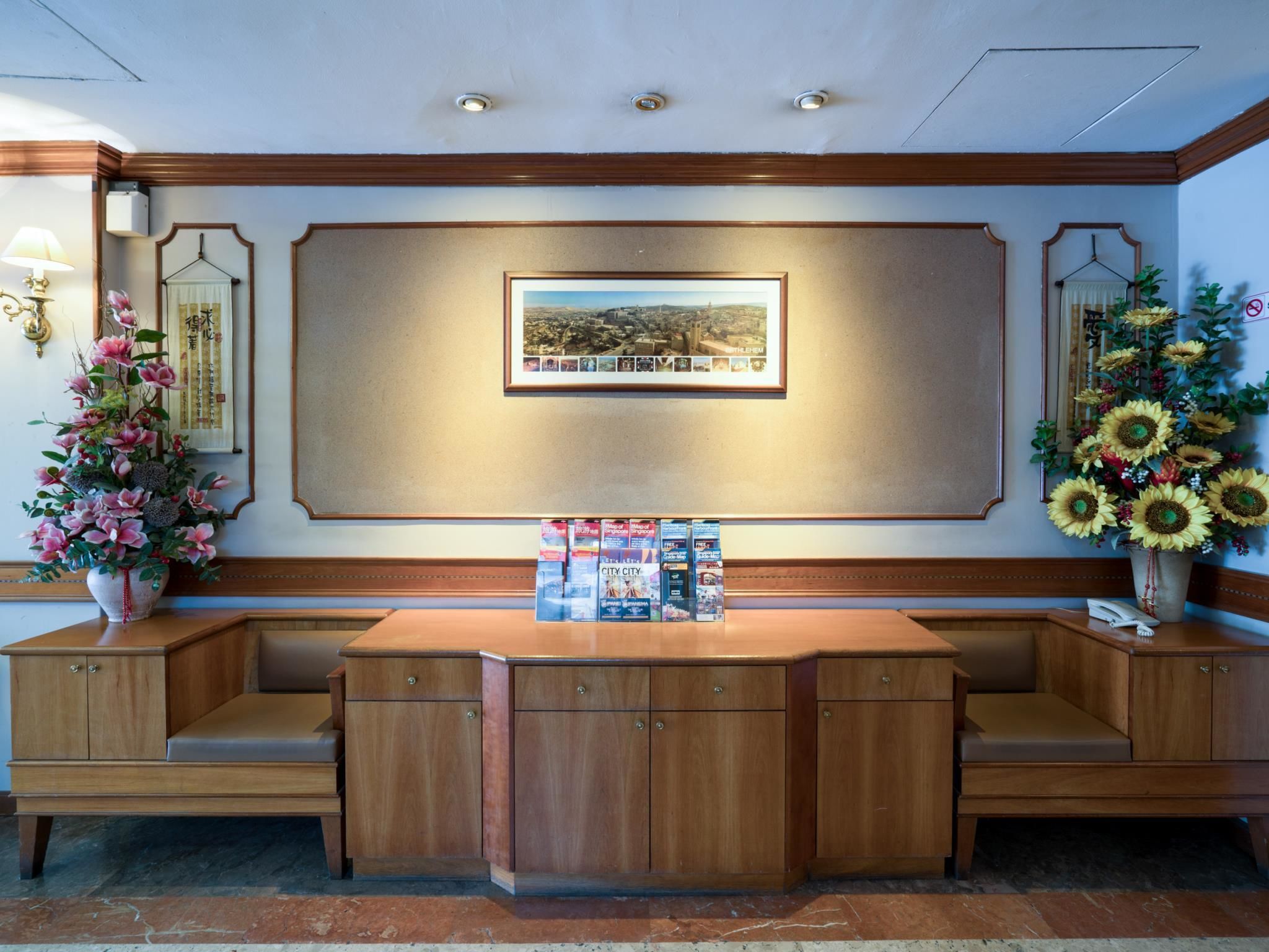 A reception desk with a framed cityscape picture, a vase of sunflowers, and a floral arrangement.